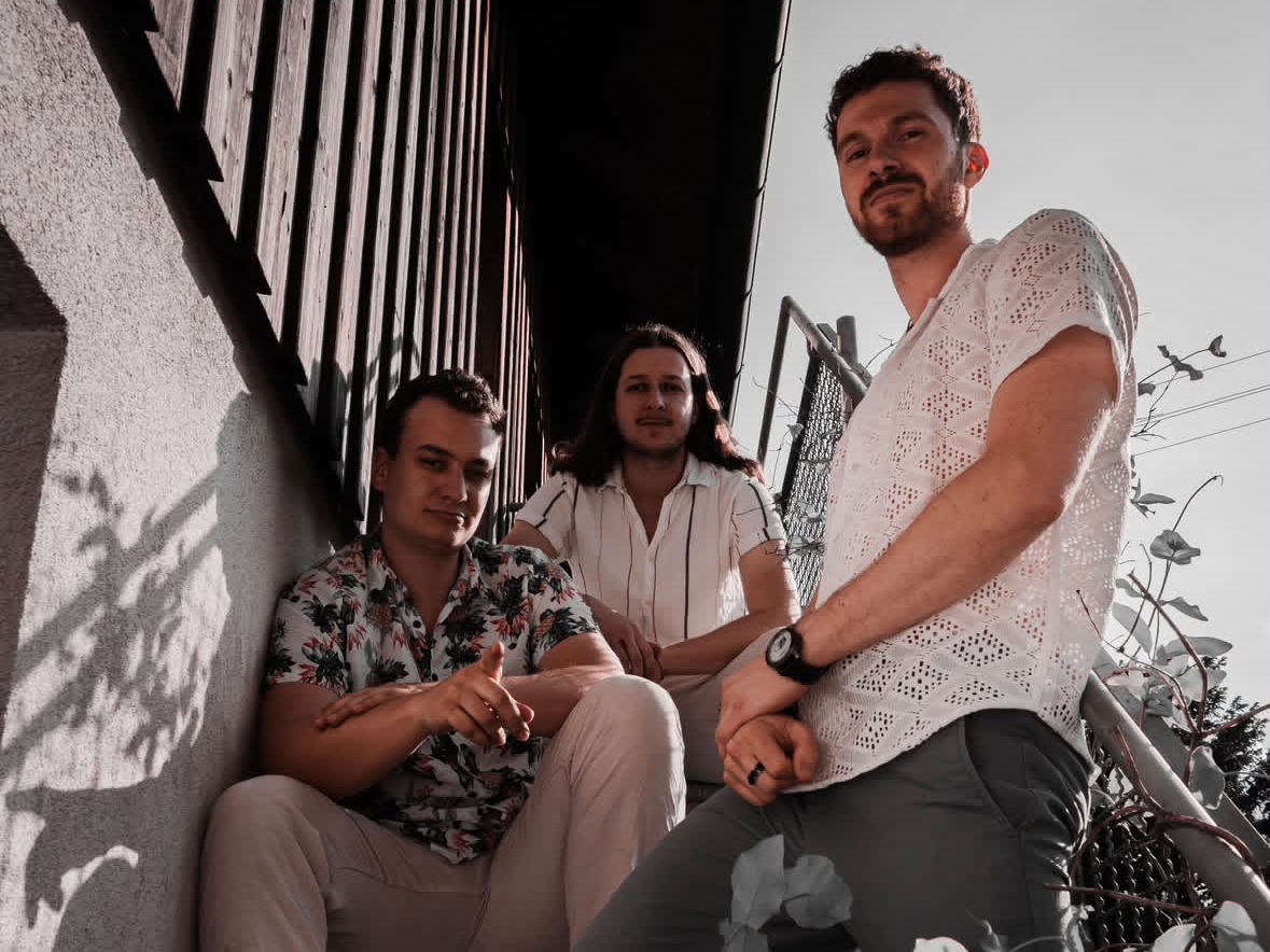 Whitefield band photo — three members sitting on an outdoor stairway in Munich, shot from a low angle in warm daylight