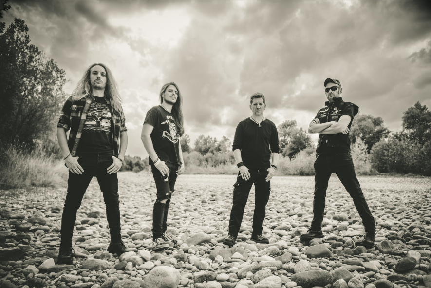 Hellgeist band promo photo — four members standing on a riverbed under a cloudy sky