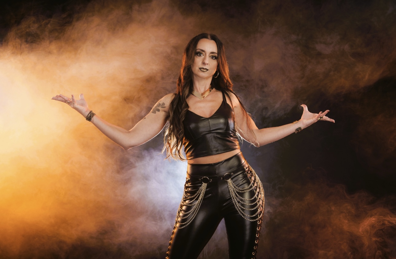 Rebel Rose vocalist Sara in black leather with arms outstretched amid orange stage smoke