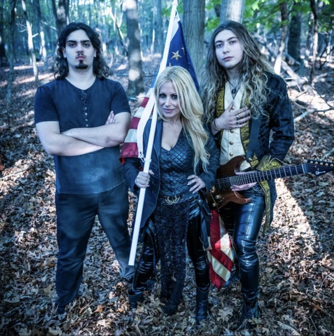 Mickey Lyxx band photo — three members standing in an autumn forest with an American flag