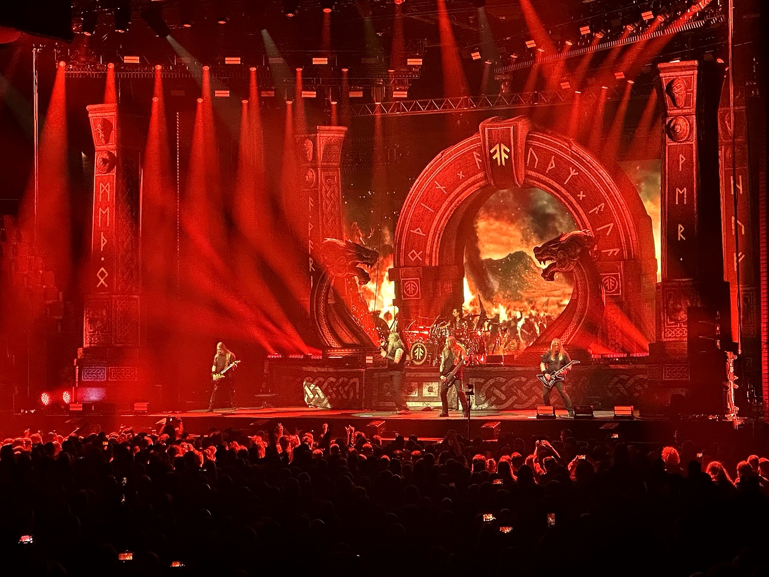 Amon Amarth performing beneath red lights and monumental Norse-inspired stage scenery at Helsinki Ice Hall.