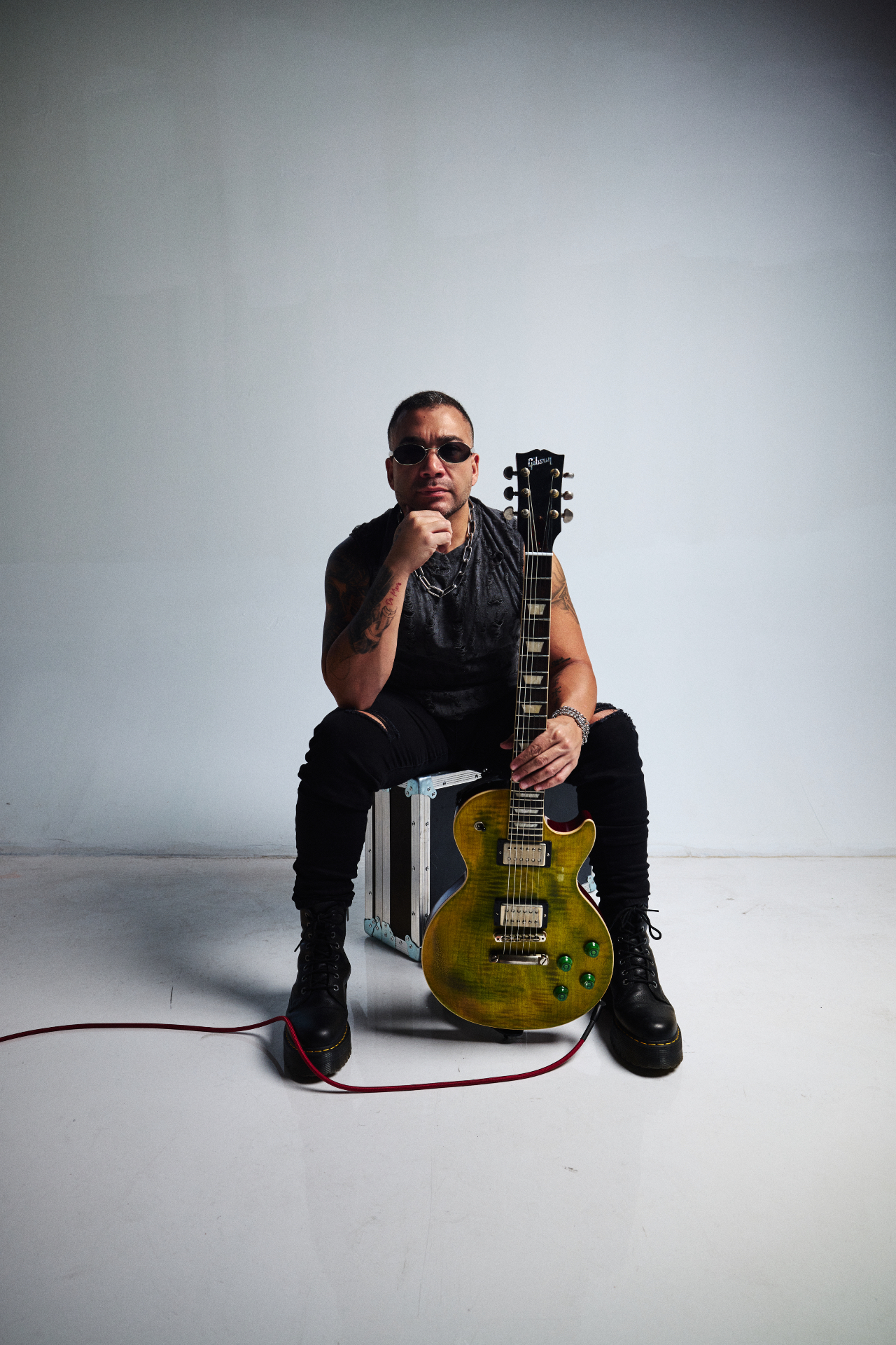Max Padron seated on a flight case holding a Gibson Les Paul with a green finish