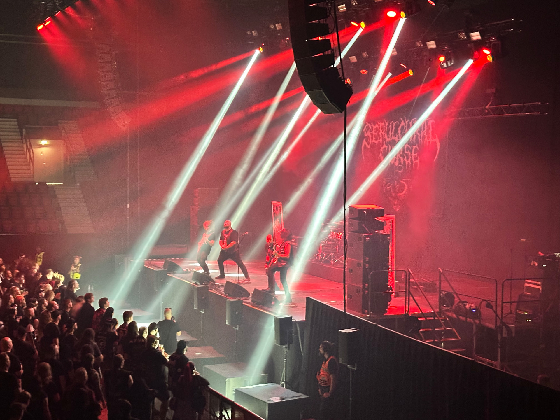 Sepulchral Curse performing indoors at Hellsinki Metal Festival 2026 in red light with white beams cutting through smoke
