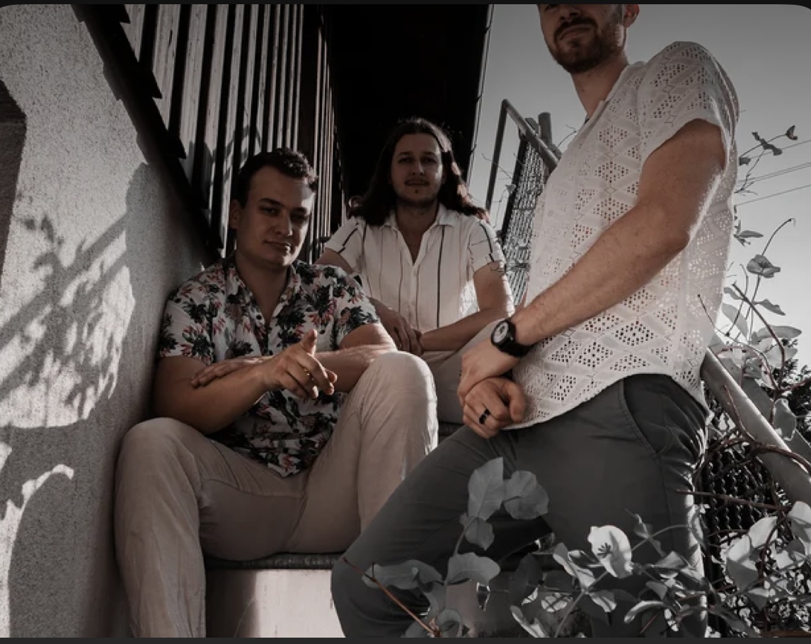 Whitefield band photo — three members sitting on an outdoor stairway in Munich, shot from a low angle in warm daylight