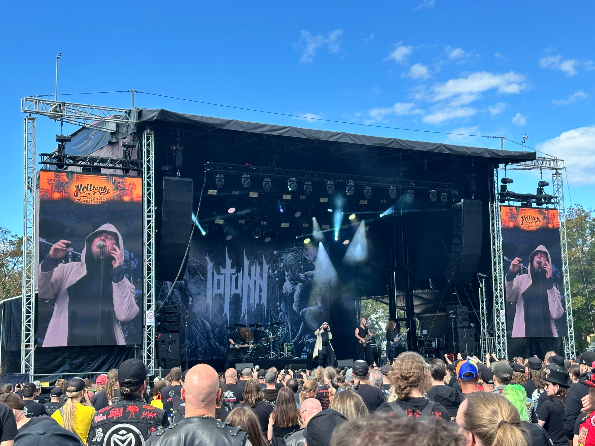 Iotunn performing at Hellsinki Metal Festival 2026 in the afternoon sun with their monochrome backdrop and a packed crowd